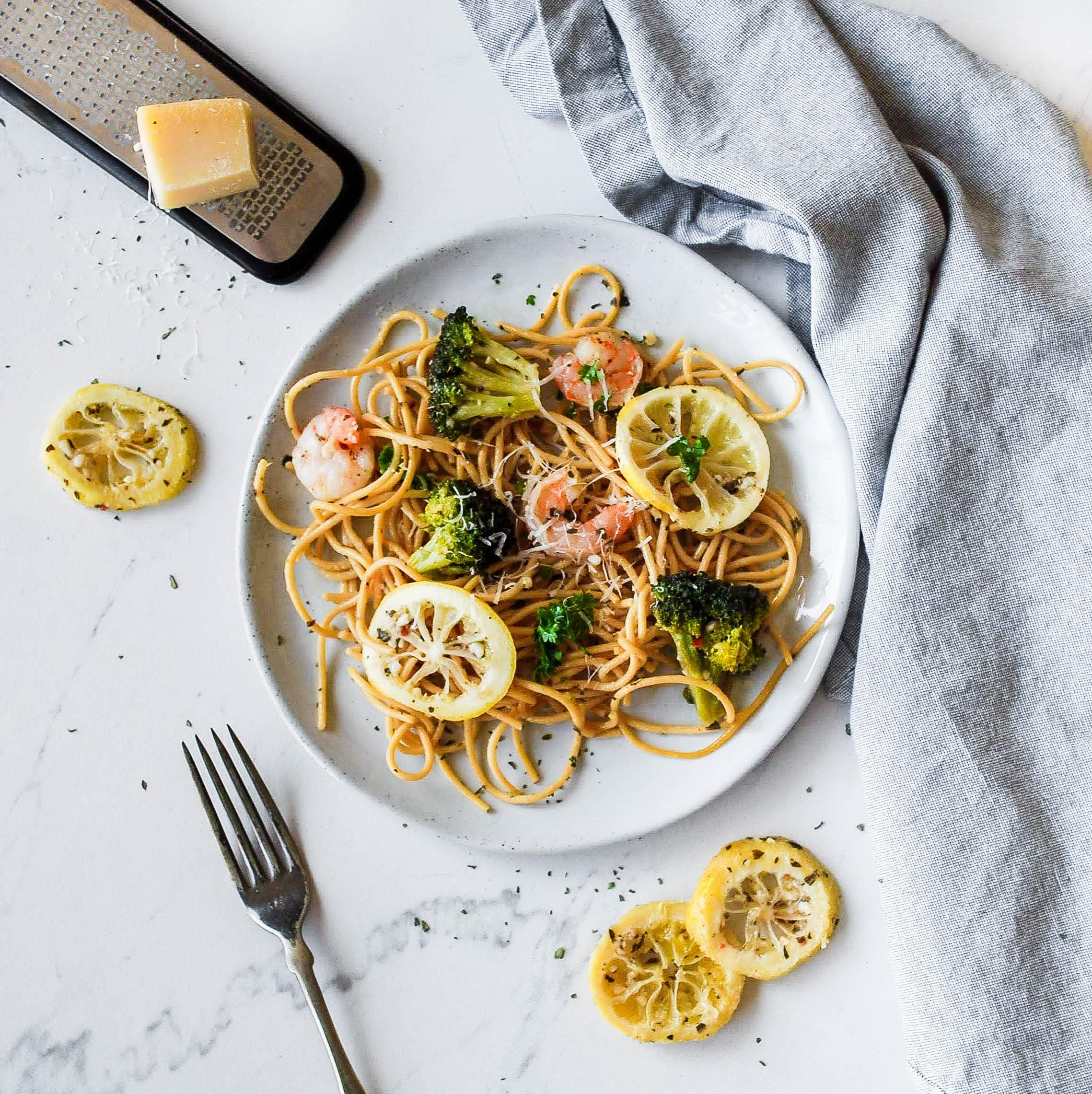 a plate of pasta, broccoli, and shrimp with lemon