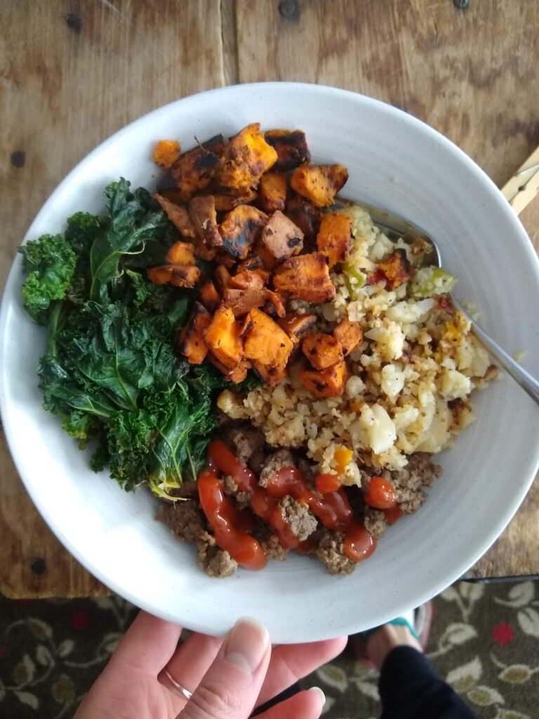 bowl with cooked kale, sweet potatoes, riced cauliflower, and ground beef with ketchup