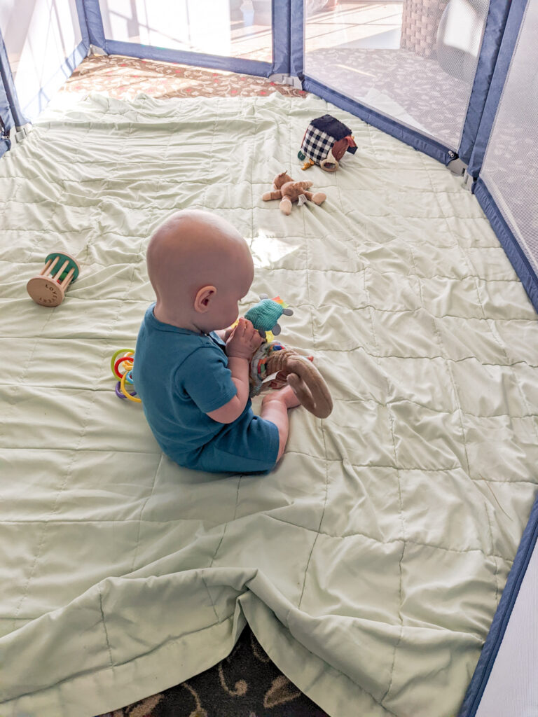 baby in a play pen with a scattering of baby toys