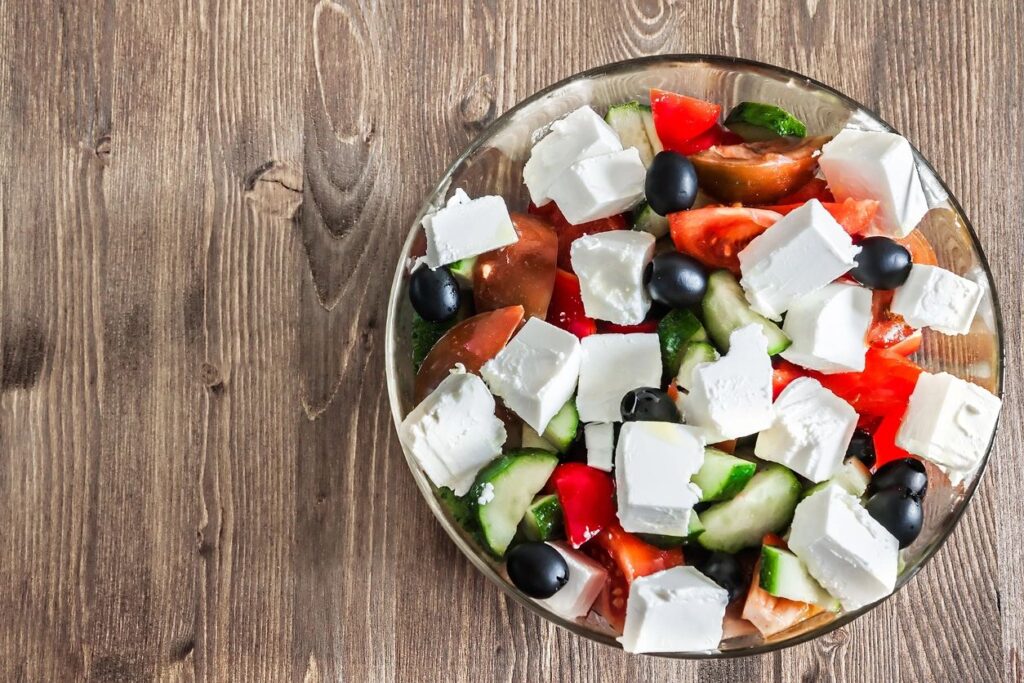 bowl with chopped cucumbers, tomatoes, whole black olives, and cubes of white cheese