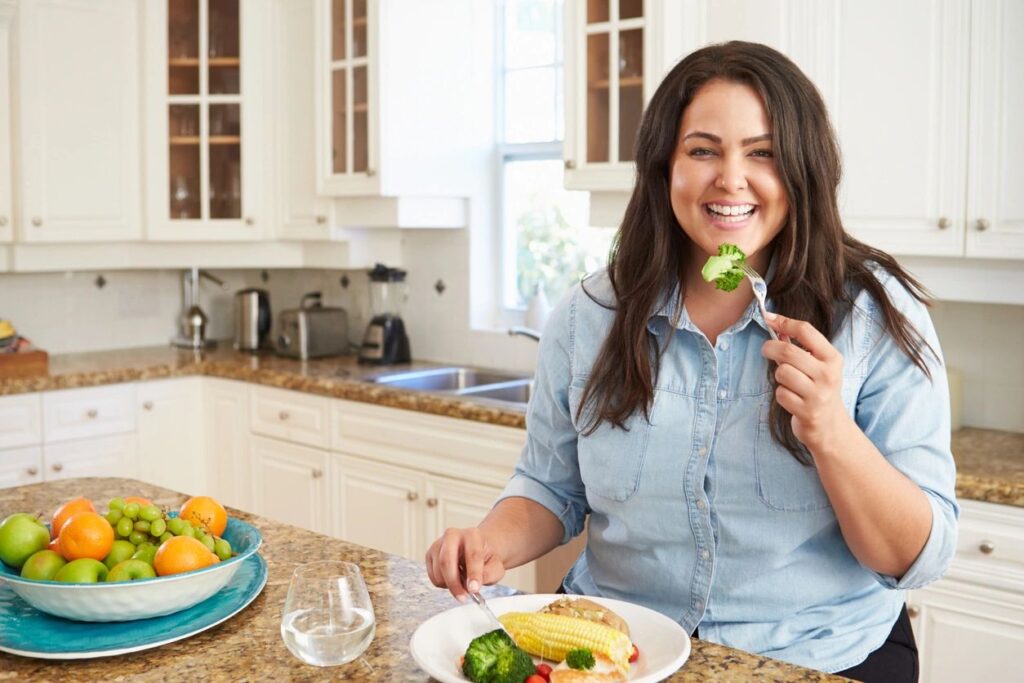 woman sitting at a kitchen island, enjoying a piece of broccoli