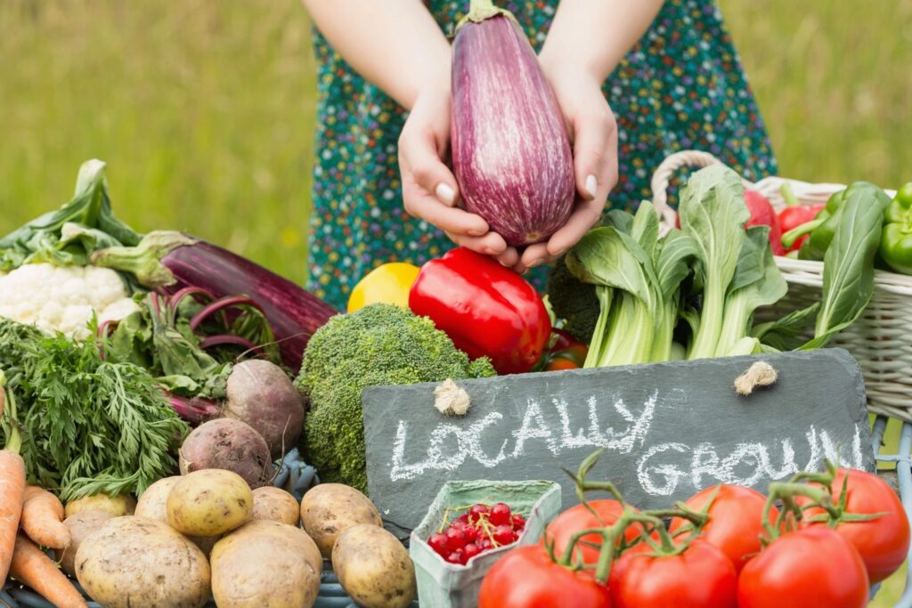 an arrangement of fresh fruits and vegetables with a sign that says "locally grown" and hands holding an egg plant