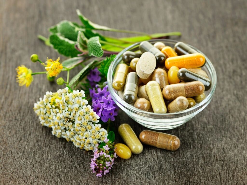 a bowl of vitamin supplements surrounded by a few herbs