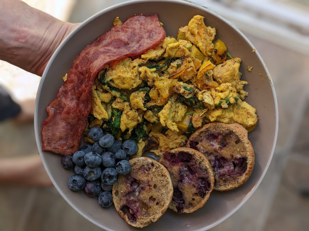 plate of food consisting of scrambled eggs with spinach, turkey bacon, blueberries, sliced homemade blueberry muffin rounds