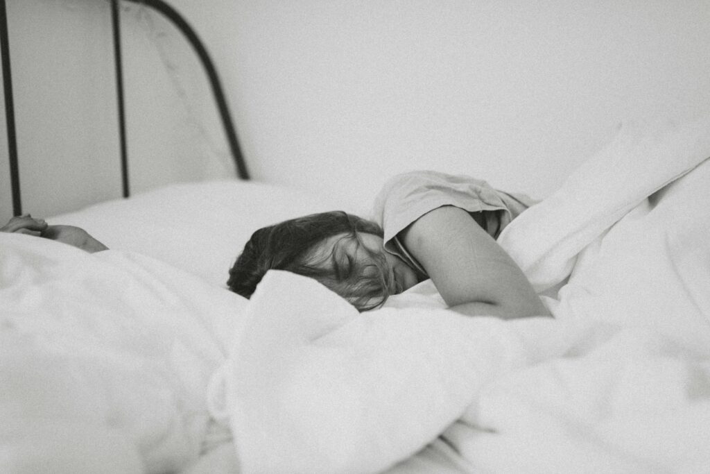 woman sleeping on her side in a bed with white sheets, arm outstretched